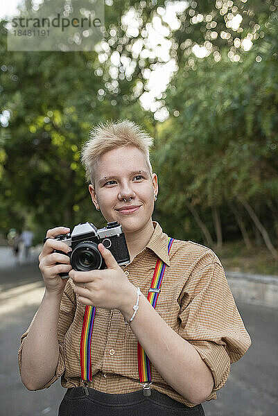 Lächelnde nicht-binäre Person mit Kamera im Park