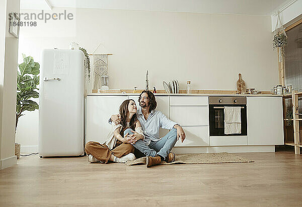Couple sitting cross-legged on floor in kitchen at home