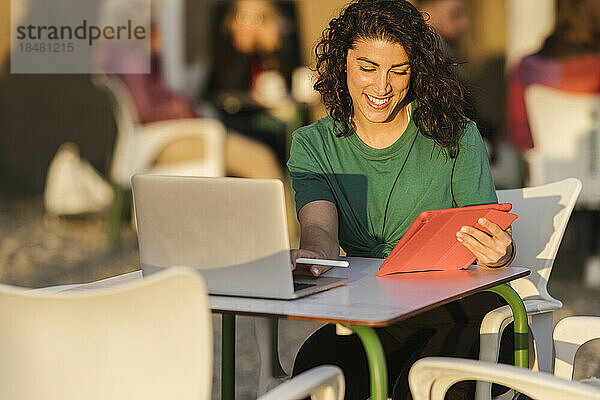 Glückliche Frau mit Tablet-PC sitzt bei Sonnenuntergang im Straßencafé