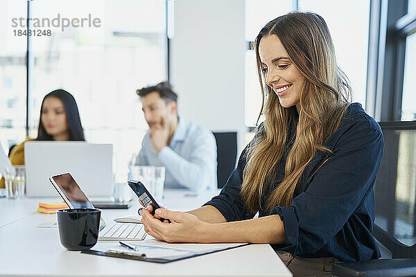 Lächelnde Geschäftsfrau benutzt Mobiltelefon am Schreibtisch im Büro