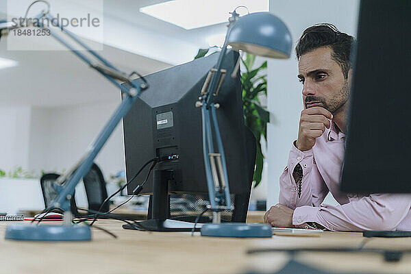 Reifer Geschäftsmann sitzt vor dem Desktop-PC im Büro