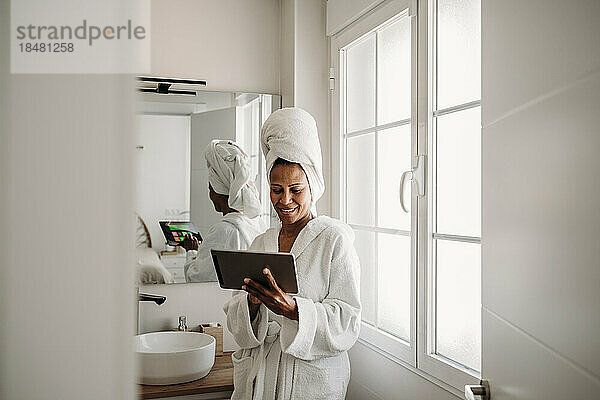Glückliche reife Frau benutzt Tablet-PC im Badezimmer zu Hause