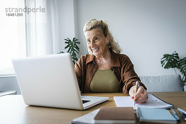 Glücklicher älterer Freiberufler  der im Heimbüro einen Videoanruf auf dem Laptop führt