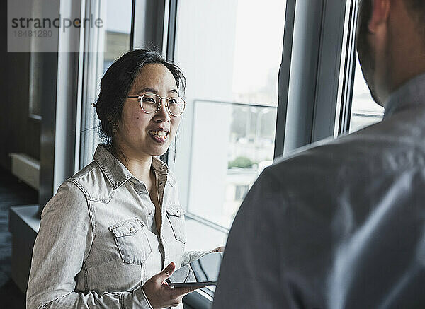 Geschäftsfrau mit Brille diskutiert mit Kollegin am Fenster im Büro