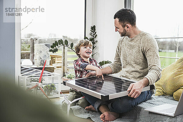 Glücklicher Sohn schaut Vater an  der zu Hause mit Solarpanel sitzt