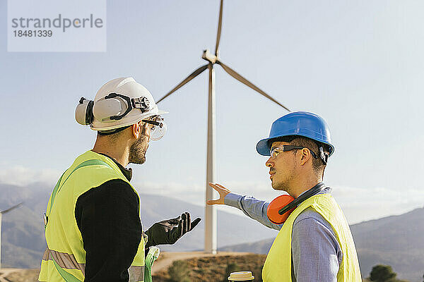 Techniker und Ingenieur diskutieren an einem sonnigen Tag über eine Windkraftanlage