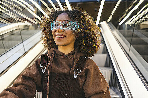 Lächelnde junge Frau mit Smart-Brille auf Rolltreppe