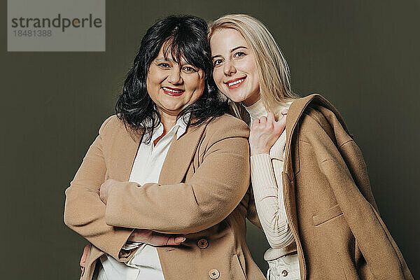 Happy mother and daughter wearing brown coat against gray background