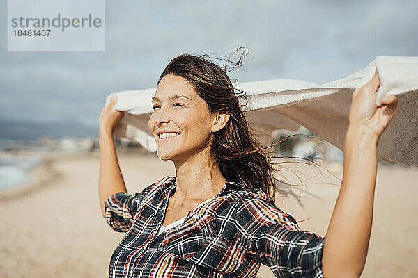 Lächelnde Frau hält Schal in der Hand und genießt den Strand