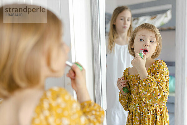 Girl applying lipstick looking in mirror at home