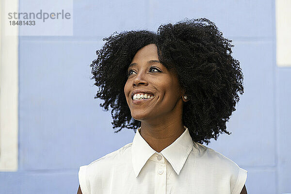 Nachdenklich lächelnde Frau mit Afro-Frisur vor der Wand
