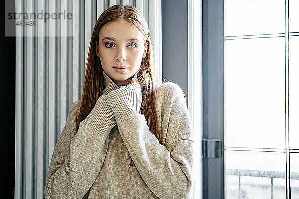 Selbstbewusstes Teenager-Mädchen trägt Pullover vor dem Fenster zu Hause