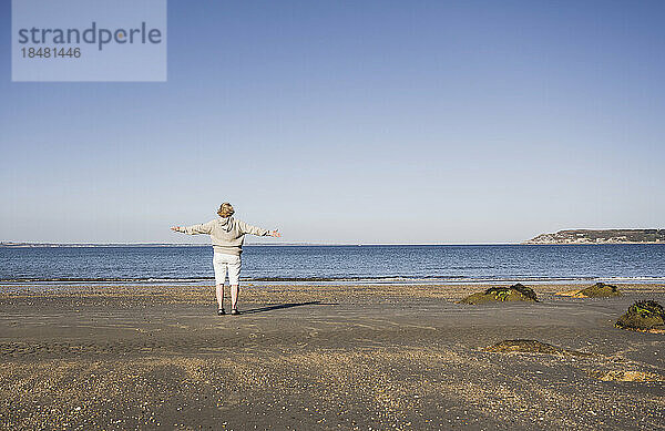Ältere Frau mit ausgestreckten Armen und bewundernd das Meer am Strand
