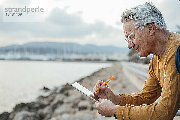Lächelnder älterer Mann benutzt Tablet-PC mit digitalisiertem Stift