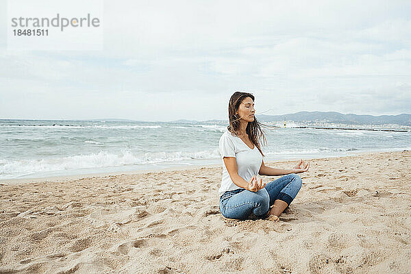 Frau macht Yoga und sitzt im Sand am Strand