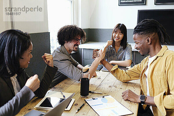 Businesswomen cheering colleagues doing arm wrestling at office