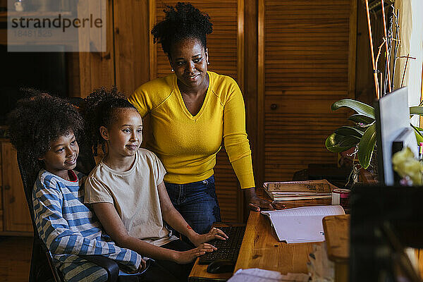 Lächelnde Frau mit Sohn und Tochter  die zu Hause den Computer benutzt