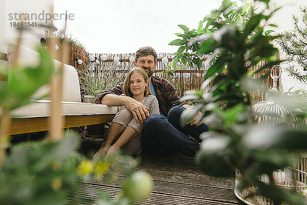 Lächelnder reifer Mann sitzt mit Tochter auf dem Balkon
