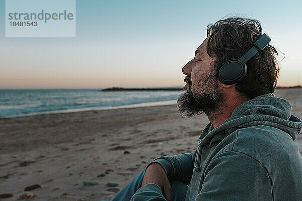 Reifer Mann mit Kopfhörern  der am Strand Musik hört
