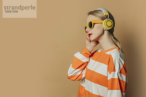 Frau mit kabellosen Kopfhörern steht vor braunem Hintergrund