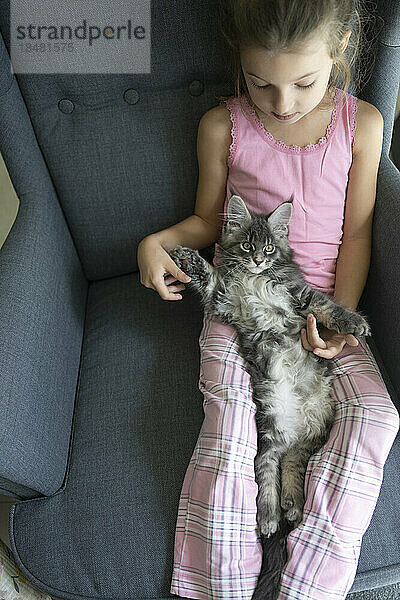 Mädchen sitzt mit Katze im Sessel zu Hause