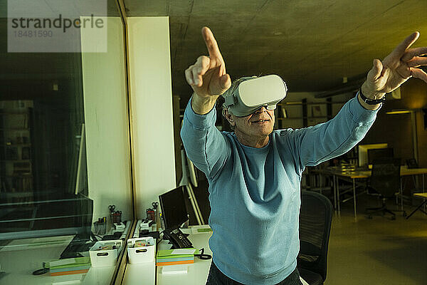 Geschäftsmann mit erhobenen Armen und Virtual-Reality-Headset im Büro