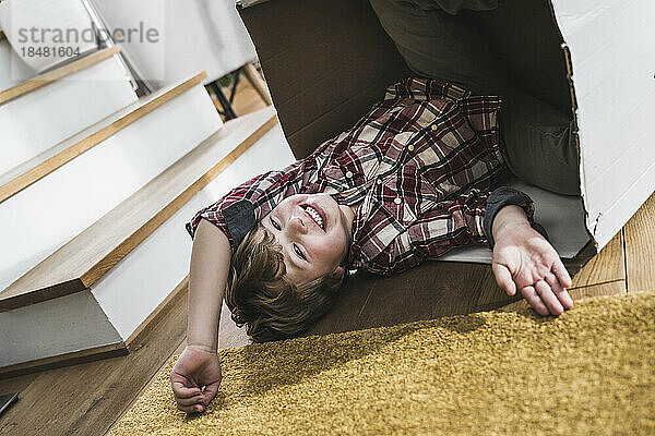 Happy boy lying on floor with cardboard box at home