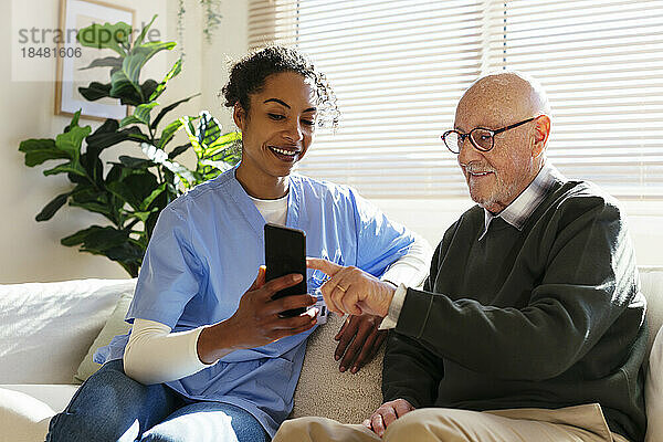 Lächelnder älterer Mann  der zu Hause sein Smartphone mit dem Hausmeister teilt
