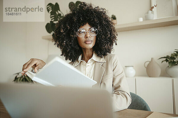 Nachdenkliche Geschäftsfrau mit Brille sitzt mit Buch im Büro