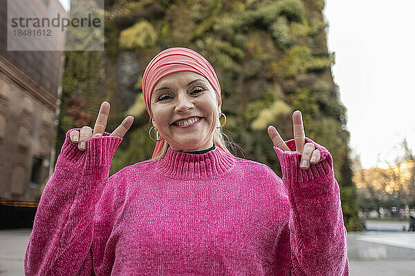 Smiling mature woman in pink sweater showing peace sign
