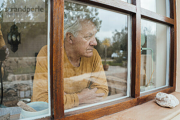 Nachdenklicher älterer Mann durch Fenster gesehen
