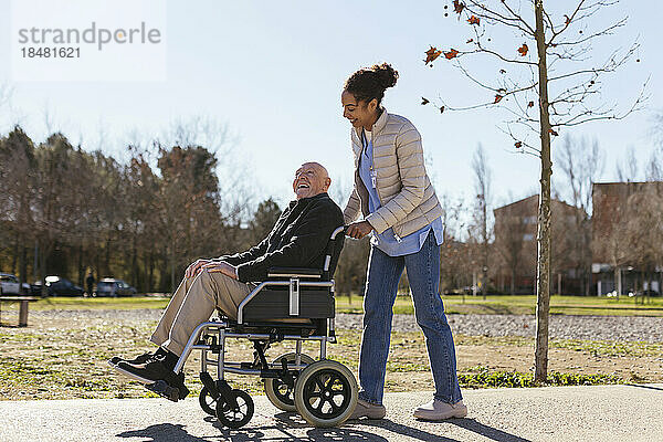 Frau hilft älterem Mann im Rollstuhl im Park