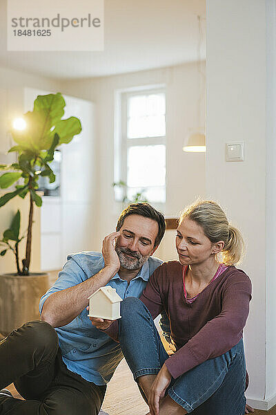 Mann und Frau sitzen zu Hause und halten ein Hausmodell in der Hand