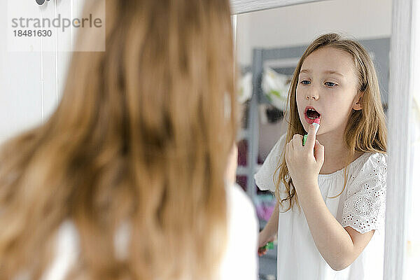 Mädchen schaut in den Spiegel und trägt zu Hause Lippenstift auf