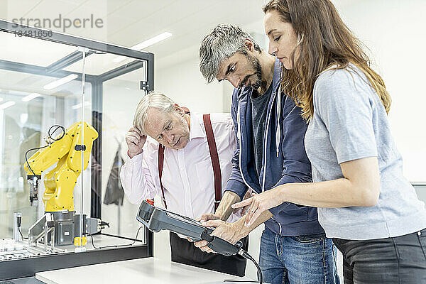 Kollegen beobachten Frau  wie sie Roboterarm mit digitaler Steuerung programmiert