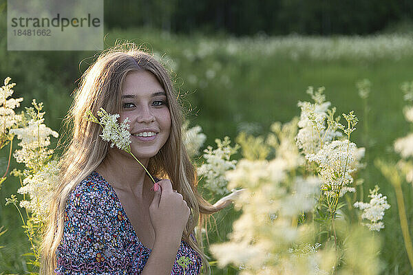 Glückliche junge Frau mit Blumen im Feld bei Sonnenuntergang