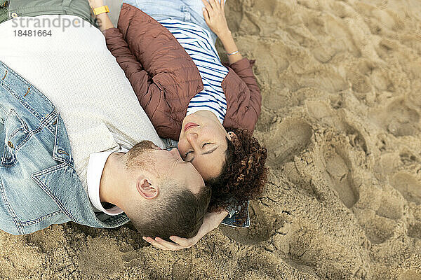Romantischer Mann und Frau liegen mit geschlossenen Augen im Sand am Strand