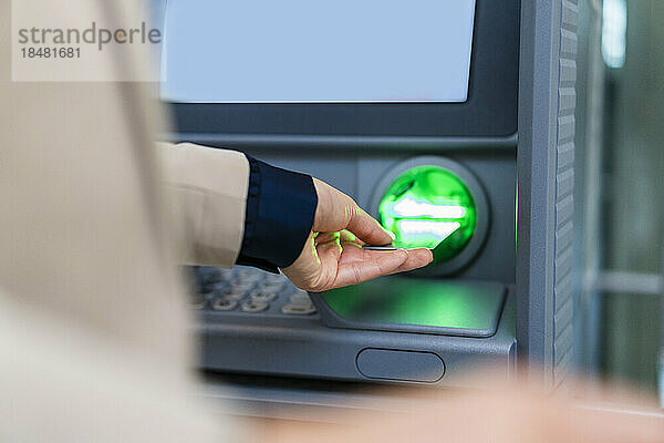 Hand einer Geschäftsfrau  die Kreditkarte in den Geldautomaten einführt