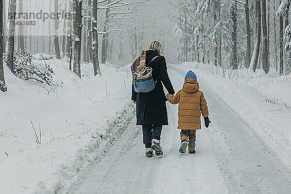 Mutter und Sohn gehen auf einem Fußweg inmitten eines verschneiten Waldes