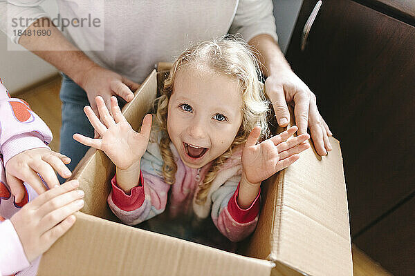 Glückliches Mädchen  das mit Schwester und Vater zu Hause im Karton sitzt