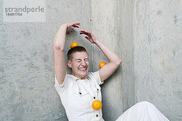 Fröhliche nicht-binäre Person  die Spaß mit Orangen vor der Wand hat