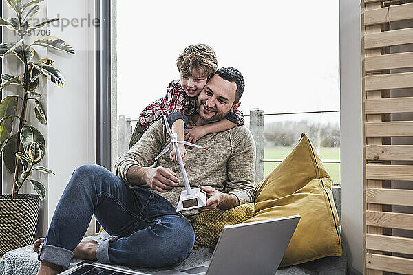 Sohn umarmt Vater  der zu Hause ein Windturbinenmodell hält