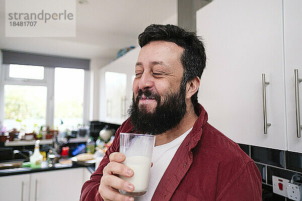 Lächelnder Mann genießt ein Glas Milch in der heimischen Küche