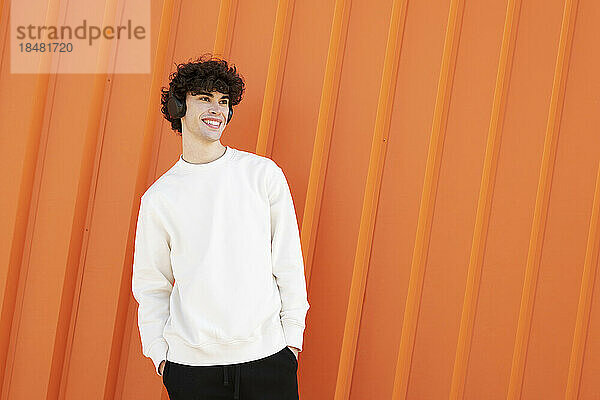 Happy man wearing headphones in front of orange wall