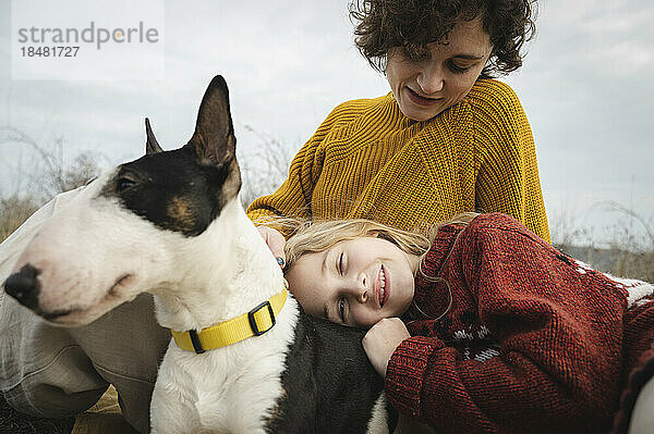 Tochter entspannt sich auf dem Schoß der Mutter mit Bullterrier-Hund