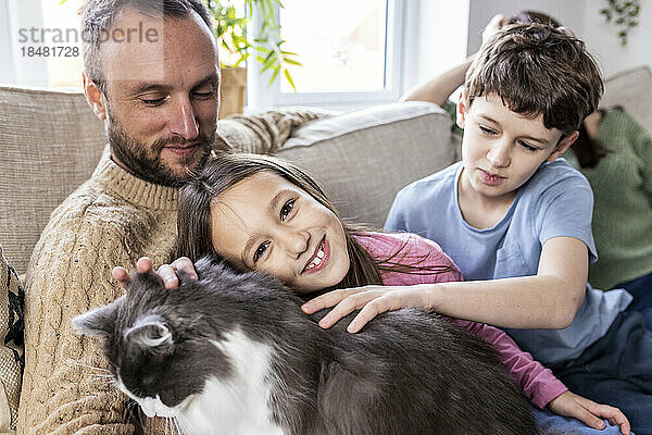 Glücklicher Vater mit Tochter und Sohn  die zu Hause auf dem Sofa eine Katze streicheln