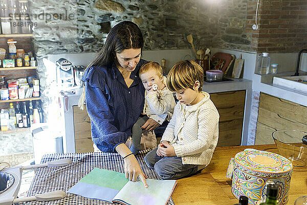 Mutter mit Kindern liest Bilderbuch in der Küche