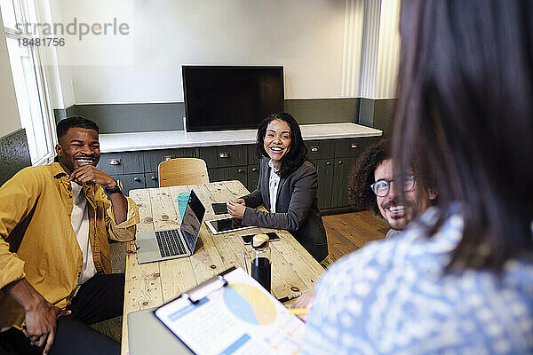 Zufriedene Geschäftskollegen sitzen bei einer Bürobesprechung am Schreibtisch