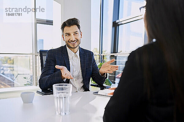 Glücklicher Geschäftsmann gestikuliert bei einem Treffen mit einem Kollegen im Büro