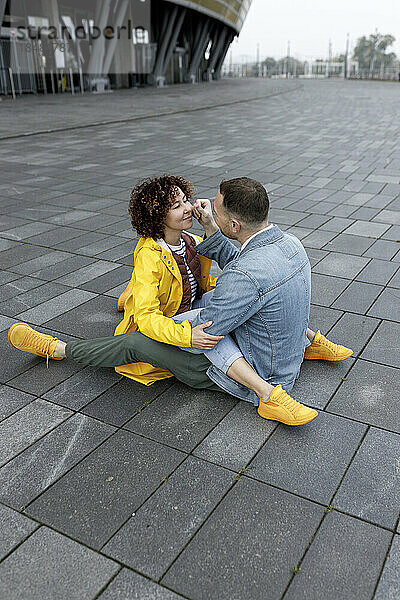 Affectionate man touching cheek of woman sitting on footpath